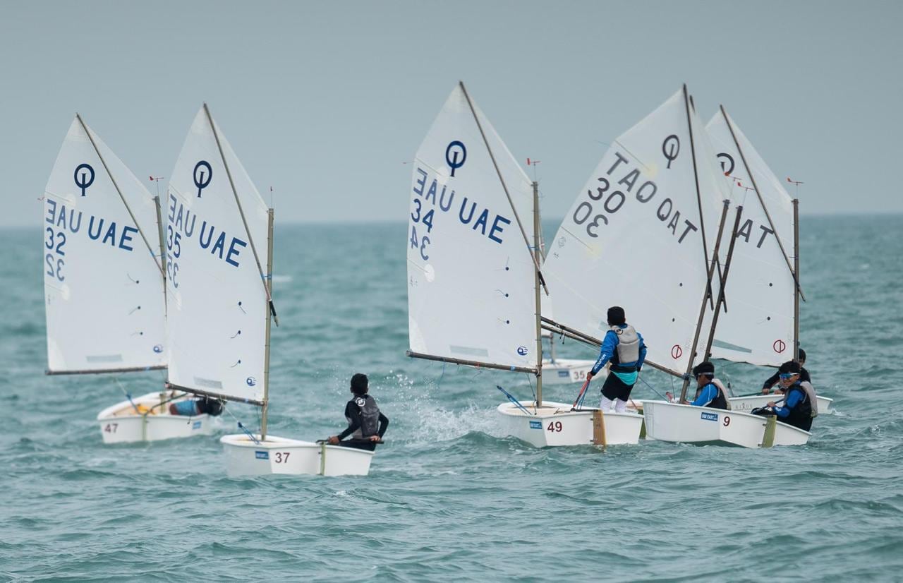 An Optimist fleet racing, with sails from the UAE and Qatar.