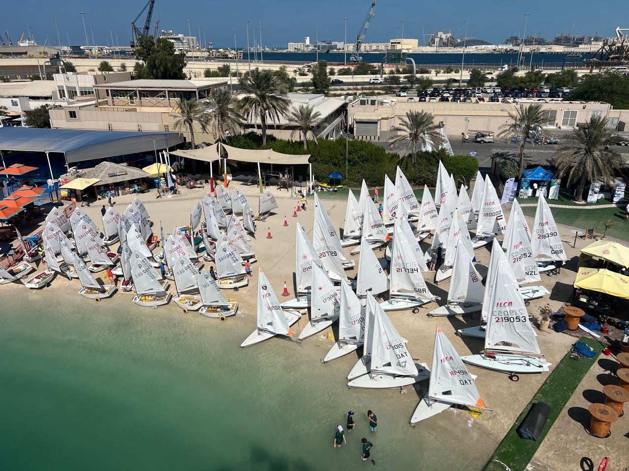 A sailing club seen from above, with dinghies rigged on the beach below the clubhouse.