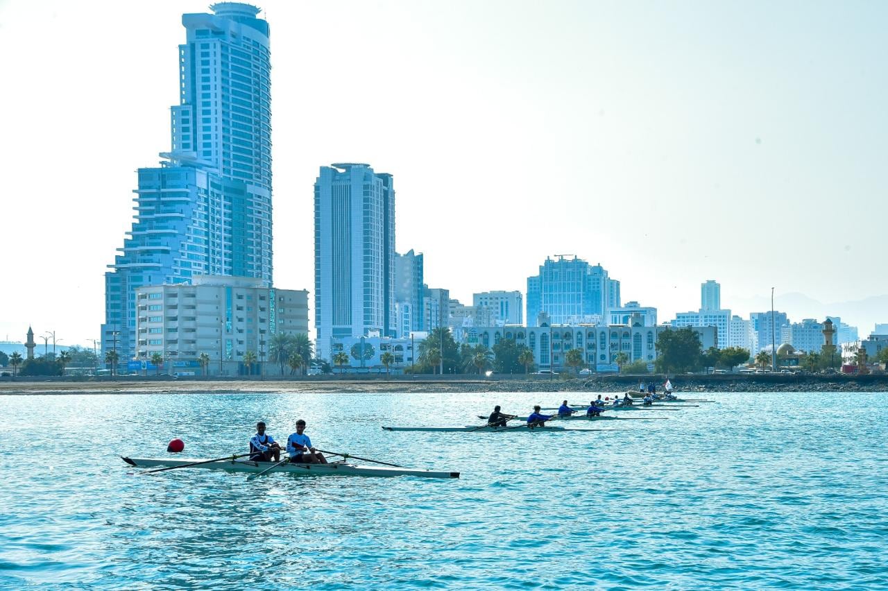 Rowing crews on calm water in front of a city skyline.